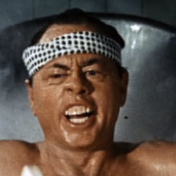 Actor Mickey Rooney portraying a Japanese man by wearing a bandana and squinting his eyes, and showing his teeth.