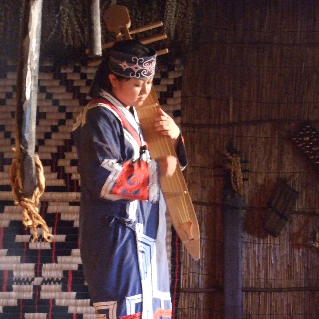 An Ainu woman playing a large wooden instrument.