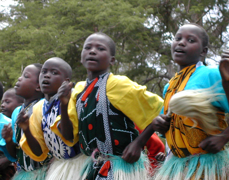Children in their early teens wearing colorful, tribal clothing while singing and dancing.