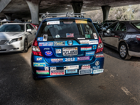 A photograph shows the back of a car that is covered in numerous bumper stickers.