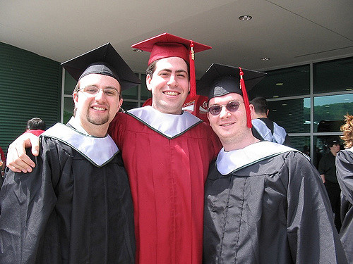 Three graduates in cap and gowns grinning