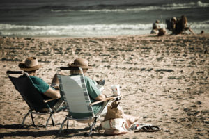 An old couple sits in chairs on a beach