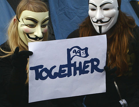 Two masked members of occupy wall street hold a sign reading 99% together