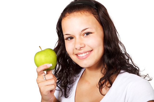 Woman smiling at camera and holding up an apple.