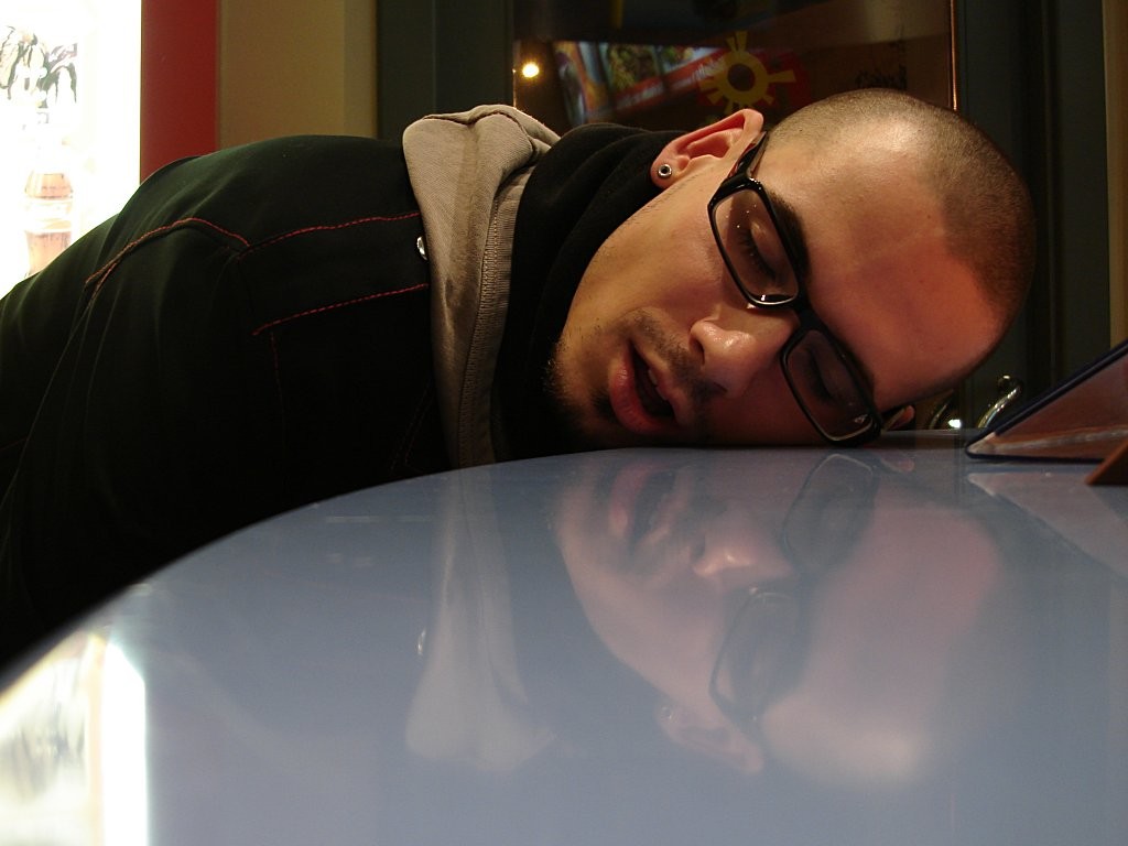 Photo of a young man asleep or "passed out." His eyes are closed and his cheek is resting on the table.