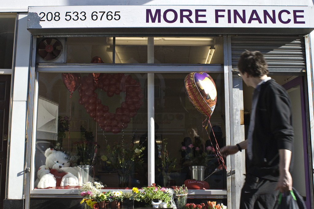 A young man walks by a shop window. A sign at the top, which has a phone number and reads, "More Finance," apparently catches his eye.