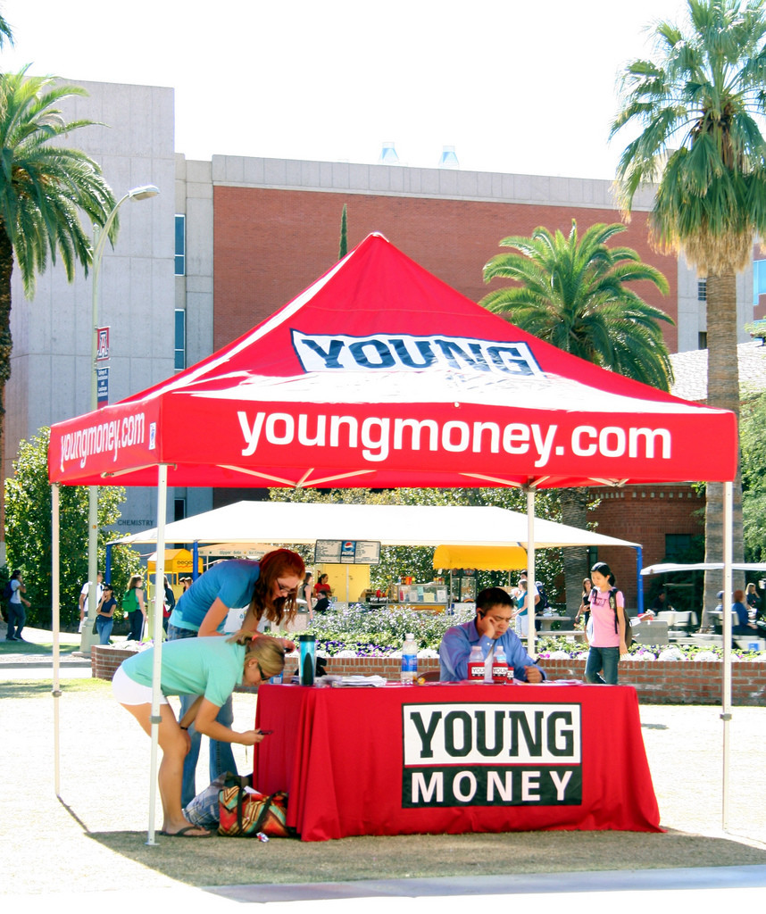 Photo of bright red "youngmoney.com" information tent staffed by several students.