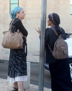 Photo of two women on street talking. Both wear dresses and head scarves.