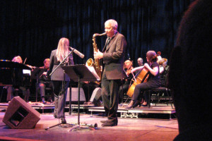 Band on stage performing. Prominent is a saxophone player.