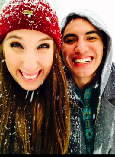 Photo of young man and woman wearing winter gear, in the snow, smiling into the camera