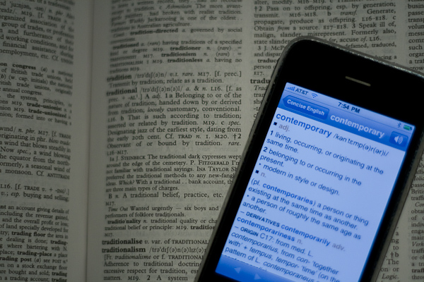 A cellphone with a dictionary page on the screen on top of a physical dictionary