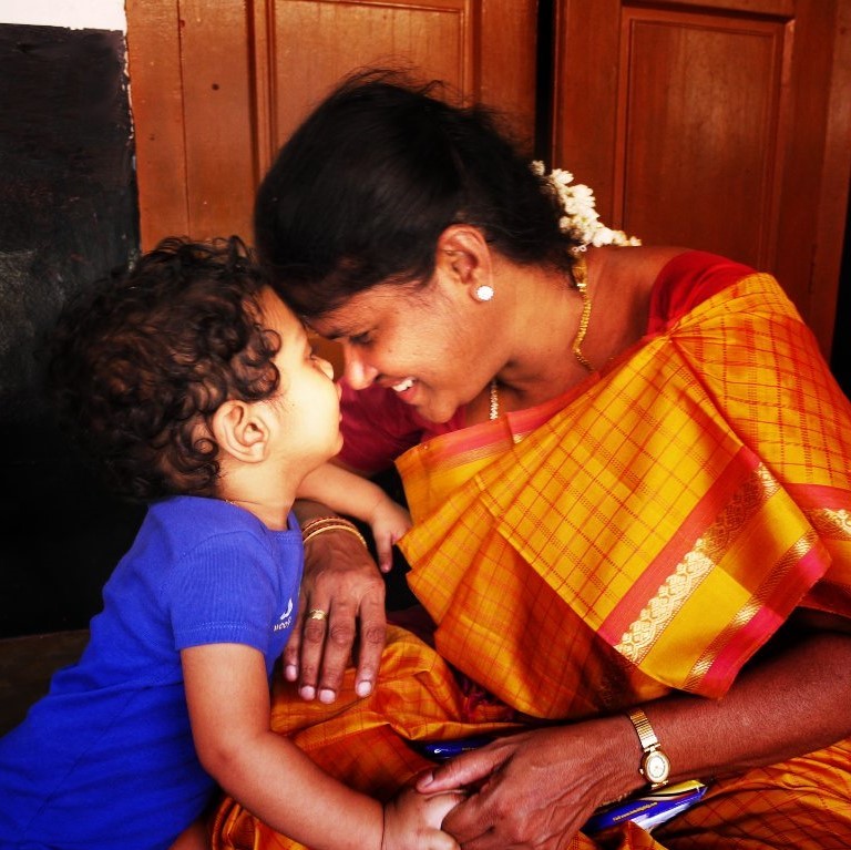 Madre sonriente asiático-india en vestido tradicional indio amarillo brillante con niño joven juntó la frente cariñosamente.