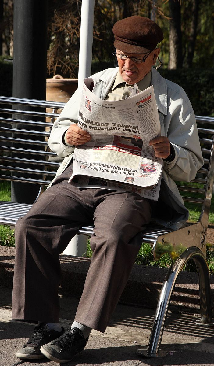 Hombre leyendo periódico en banco del parque.