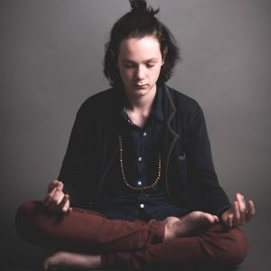 Un joven se sienta en la posición de loto meditando.