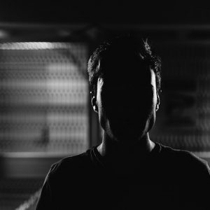 Un hombre se para en una habitación oscurecida con el rostro casi completamente oscurecido por la sombra.