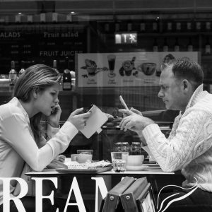 Un hombre y una mujer se sientan uno frente al otro en una mesita en una cafetería. Ambos están mirando su propio teléfono inteligente en lugar de interactuar entre ellos.