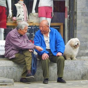 Dos hombres mayores se sientan juntos frente a una tienda conversando.