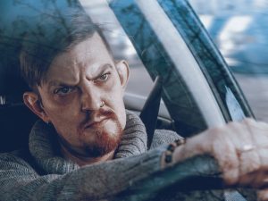 Un hombre con una expresión enojada en su rostro se sienta al volante de un automóvil mirando hacia adelante.