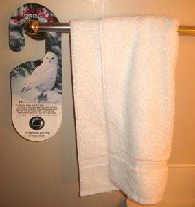 Un toallero en el baño de visitas de un hotel tiene una toalla blanca colgada junto a un letrero informativo sobre cómo ahorrar agua.