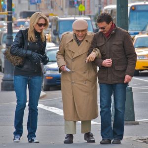 Un hombre y una mujer más jóvenes que ayudan a un señor anciano por la calle.