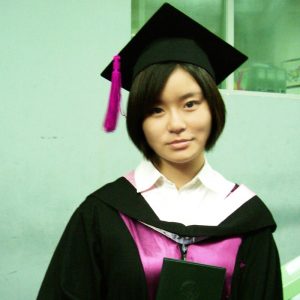 Una mujer del este de Asia vestida con una gorra y un vestido de graduación lleva una expresión neutra o tenue.