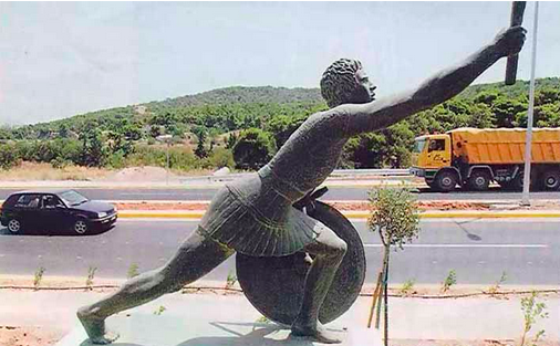 Bronze statue of Pheidippides standing beside a road.