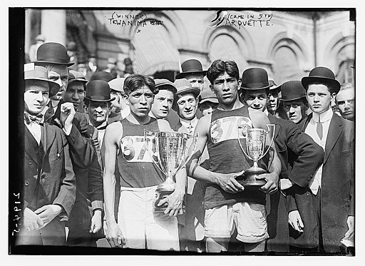 Photograph of crowd at the end of the May 6, 1911 New York City marathon, with Hopi American long distance runner and Olympic medal winner Louis Tewanima and Mitchell Arquette, member of the cross country team of Carlise Indian School, in the foreground holding trophies.
