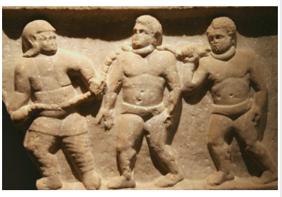 Relief carving in a stone Roman wall, showing three slaves collared and chained together.