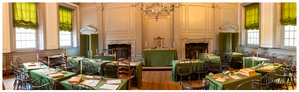 Photograph of the Assembly Room in Independence Hall, showing rows of tables and chairs facing a central podium.