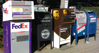 A row of metal mailboxes, for the following services from left to right: FedEx, the University of California mail system, UPS, and the US Postal Service.