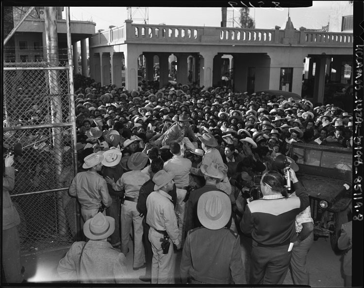 Black-and-white photograph of a crowd of Braceros at the California-Mexico border, 1954.