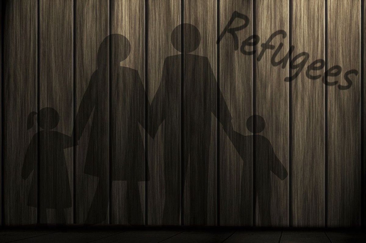 The shadows of a man, a woman, and two children, all holding hands, cast on a wooden wall.