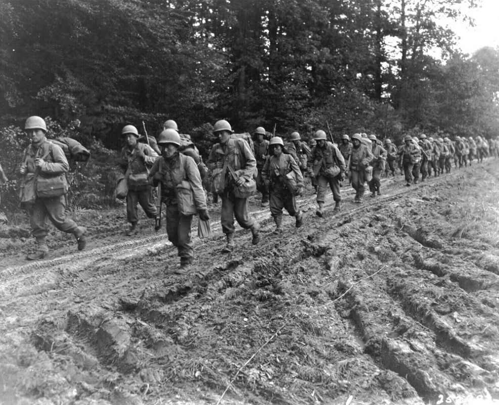 A group of Japanese-American infantrymen make their way up a muddy country road.