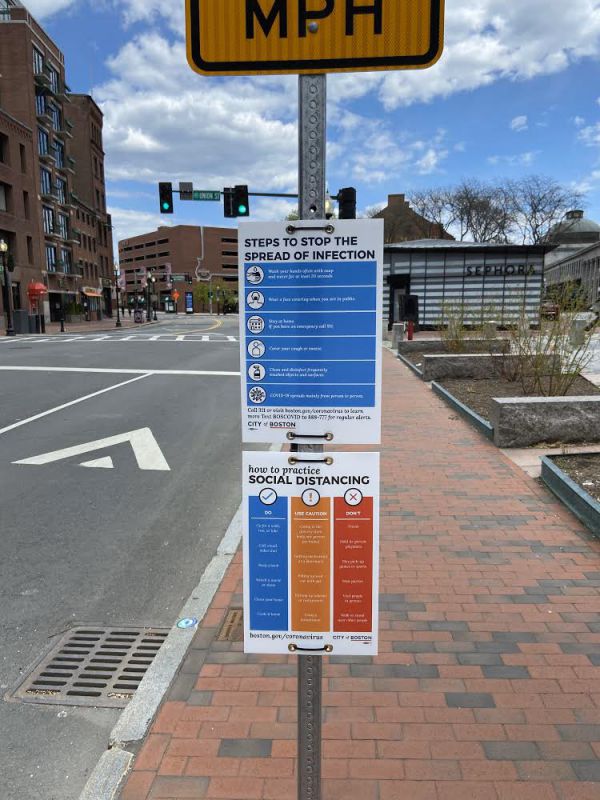Plastic signs instructing people how to practice social distancing during the COVID-19 pandemic, attached to a traffic sign on a Boston street.