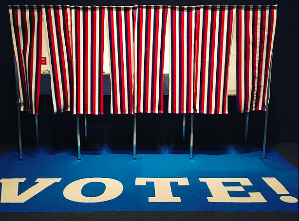 A row of US voting booths with curtains in a red, white and blue stripe pattern.