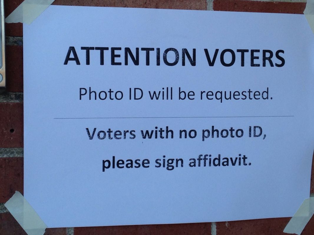 A computer printout taped on the window of a New Hampshire polling place, stating "Attention Voters: Photo ID will be required. Voters with no photo ID, please sign affidavit."