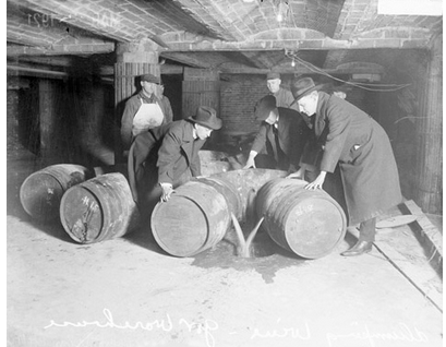 Black-and-white 1921 photograph of Prohibition-enforcement agents in a cellar, destroying barrels of alcohol by pouring the contents onto the ground.