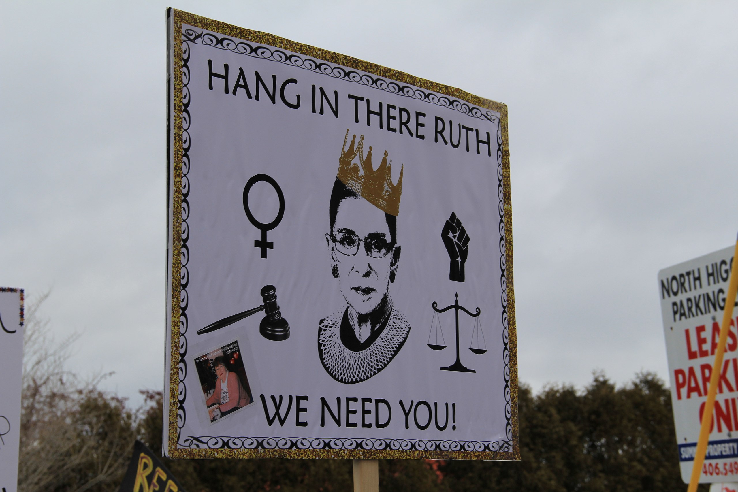 Photograph taken at a 2018 Women's March in Missoula, Montana, showing a sign with a graphic of Supreme Court Justice Ruth Bader Ginsberg in a crown and the words "Hang in there Ruth, we need you!" Photograph taken by Wikimedia user Montanasuffragettes. 