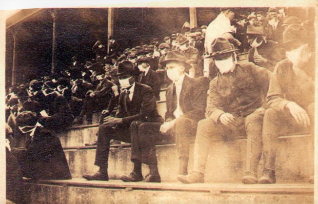 Black-and-white photograph of the stands at a Georgia Tech football game in 1918, during the Spanish Flu. Almost all visible spectators have mouths and noses covered with masks made out of a pale fabric.