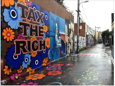 Photograph of a mural entitled "Tax the Rich" painted by Megan Wilson in Clarion Alley, San Francisco. Mural consists of a dark brown background mostly covered by flowers in varying shades of orange, blue, and purple, overlaid with the phrase "Tax the Rich" written in black capital letters outlined with red and white.