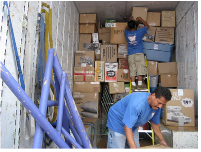 Photograph of two employees from a moving company loading a moving van. Photograph taken in 2010 by Rharel1.