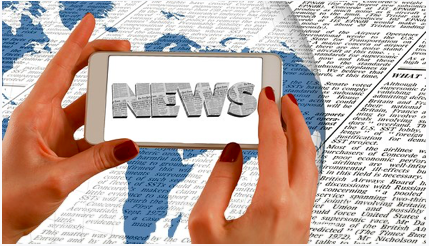 Graphic of the globe is superimposed on a newspaper background; a person's hands hold a smartphone towards the globe, with the phone screen showing the word "NEWS" formed from newsprint.