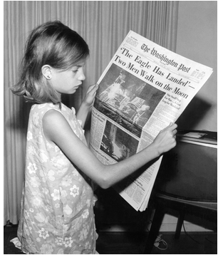Black-and-white photograph of a girl holding the Washington Post from Monday, June 21, 1969, with the headline "'The Eagle Has Landed'‍—‌Two Men Walk on the Moon." Photograph by Jack Weir.