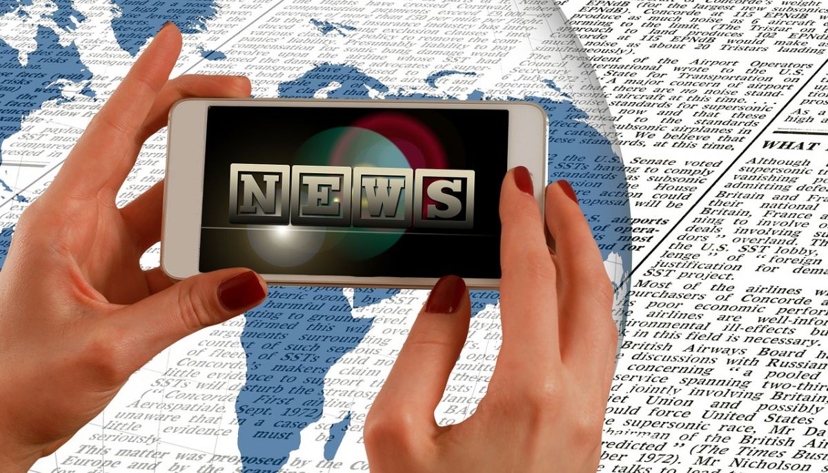Image consisting of a background of newsprint partially overlaid by a graphic of the globe, and a foreground of a pair of hands holding a smartphone whose screen shows the word "NEWS."