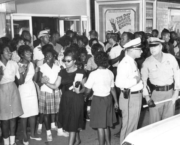 Fotografía en blanco y negro de 1963, que muestra una manifestación de derechos civiles frente a una sala de cine segregada en Tallahassee, Florida.