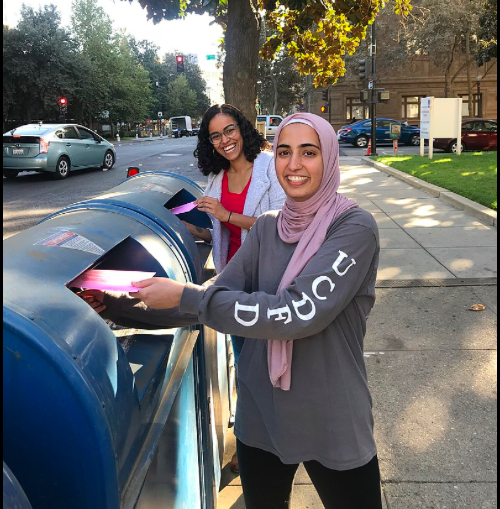Photograph from 2018, showing two women from the League of Women Voters of California placing mail-in ballots into mail drop-off boxes.