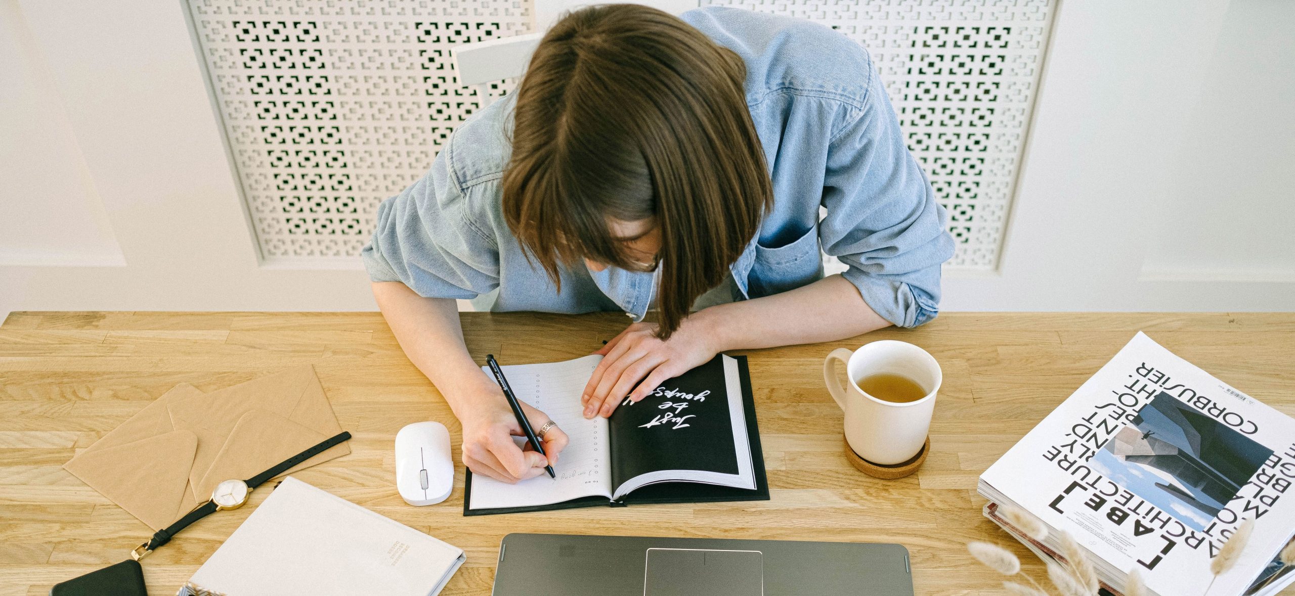 Mujer escribiendo notas en cuaderno delante de laptop