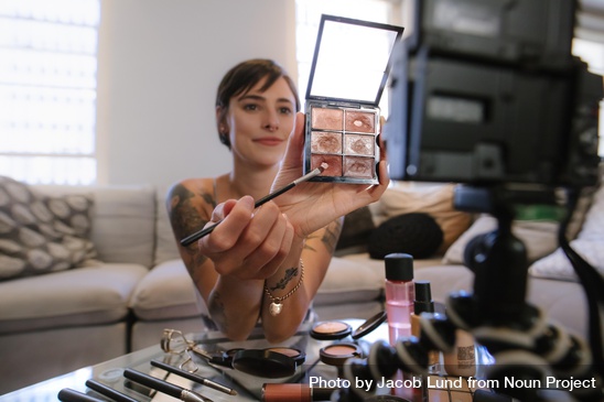 A woman holds up a makeup pallet to a camera. 