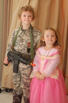 A brother dressed in a camouflage military uniform holding a toy gun with his sister dressed in a pink princess dress