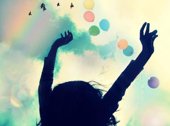 The shadowed outline of a young person with her hands raised in the air while colorful balloons and birds float and fly above.